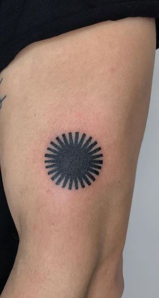 Blackwork style sun tattoo on the right upper arm